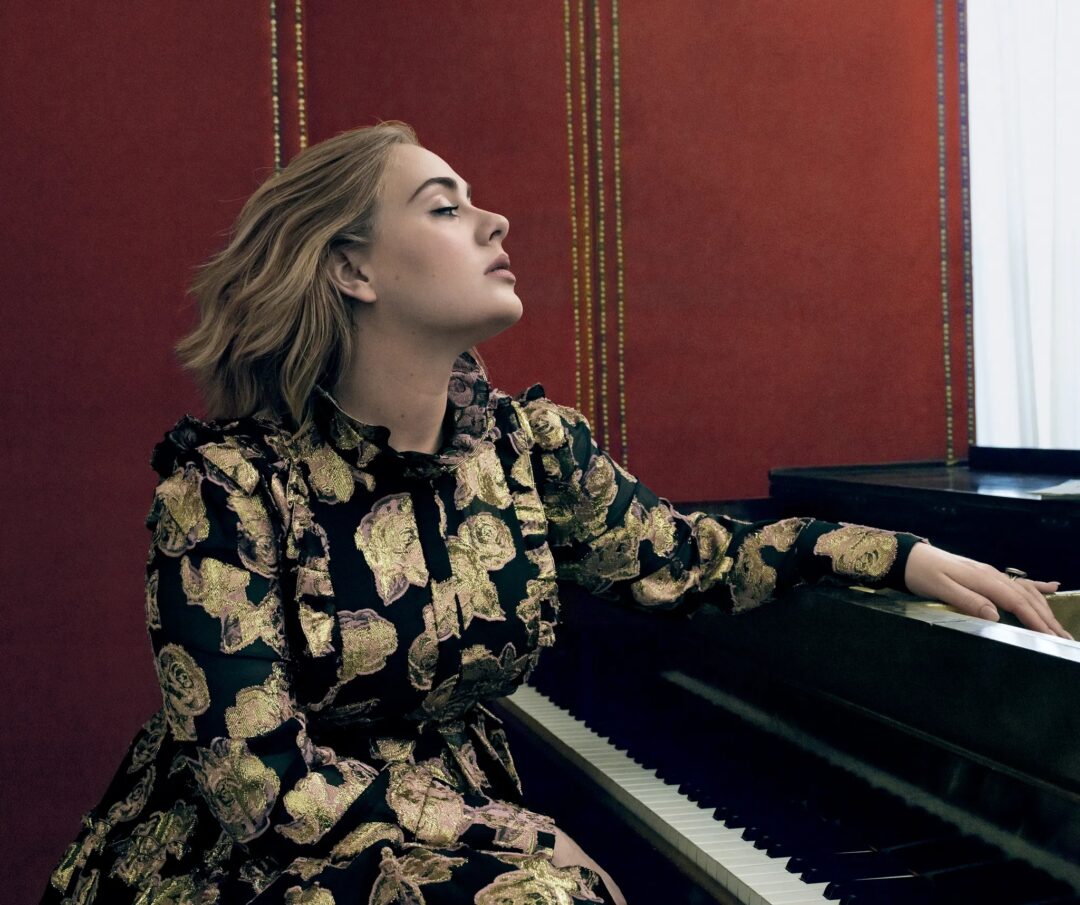 Adele in profile at a grand piano against a red wall, Erdem dress, by Annie Leibovitz for Vogue