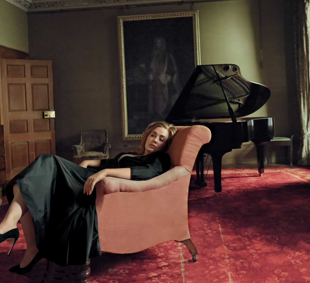 Adele reclining in a pink armchair beside a grand piano at Claridge's, Giambattista Valli dress